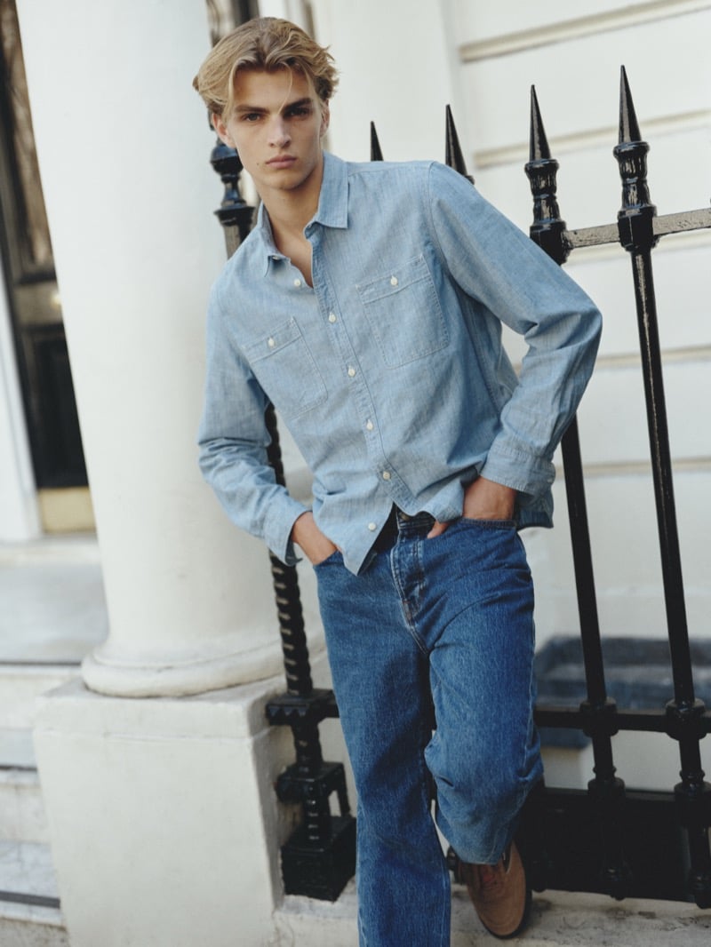 Maurits Scheij in a chambray shirt with flap pockets leaning against a wrought iron fence