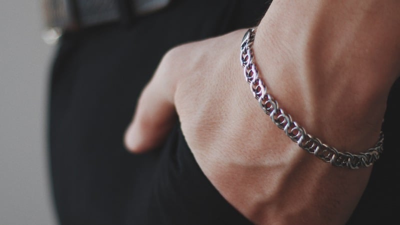 Close-up of a man's hand in his pocket wearing a twisted silver chain bracelet