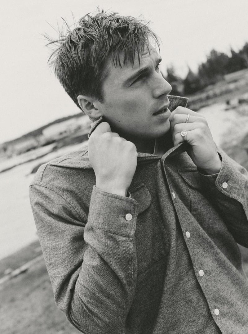 Black-and-white close-up of a man adjusting the collar of a wool overshirt on a windy beach, for Taylor Stitch Fall 2026