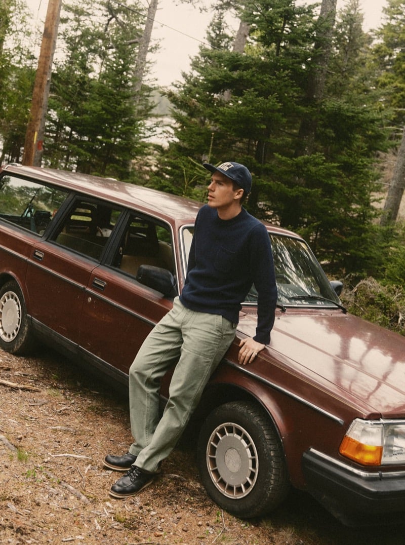 Man in a navy sweater and green cargo pants leaning against a vintage station wagon in the woods, for Taylor Stitch Fall 2026