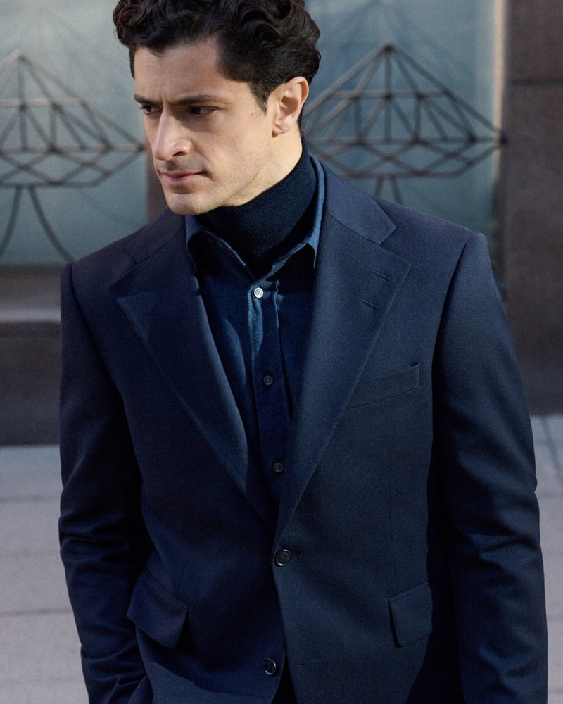 Close-up of Cyrus Amini in a navy suit jacket and turtleneck with a collared shirt underneath