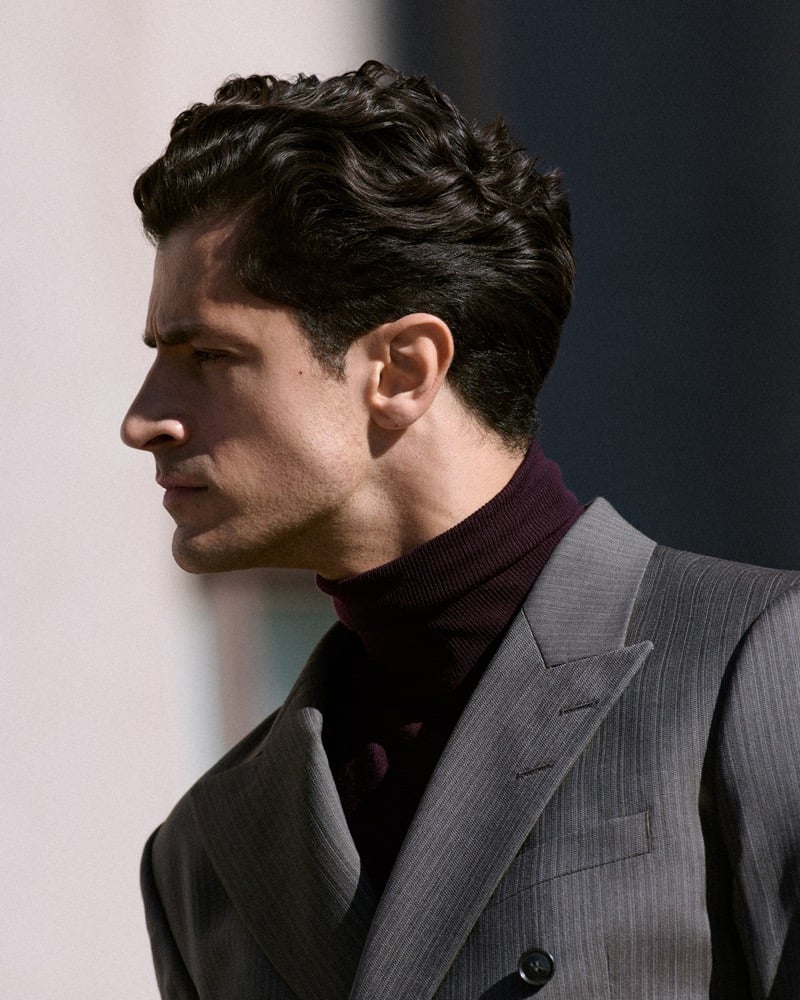 Close-up profile of Cyrus Amini in a gray double-breasted suit and a burgundy turtleneck