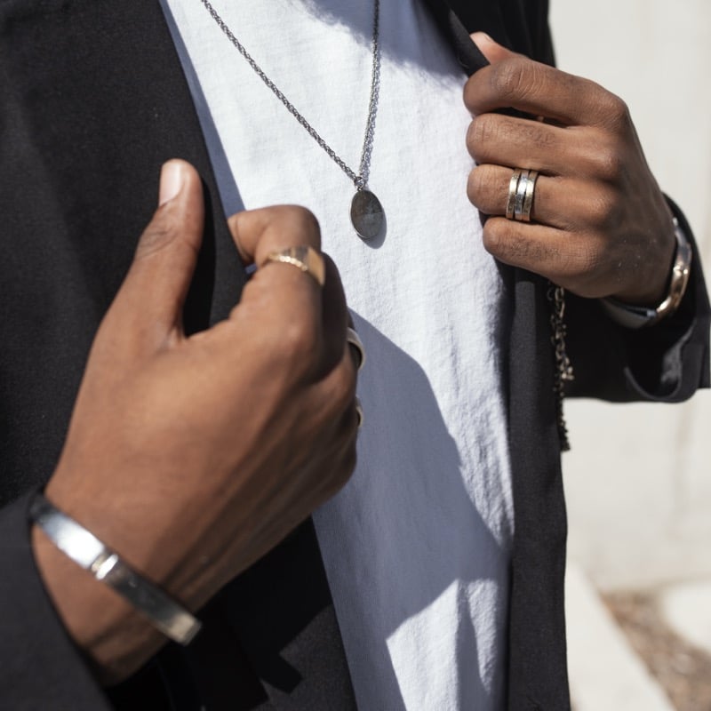 A man wearing a titanium-toned bar bracelet along with layered silver necklaces