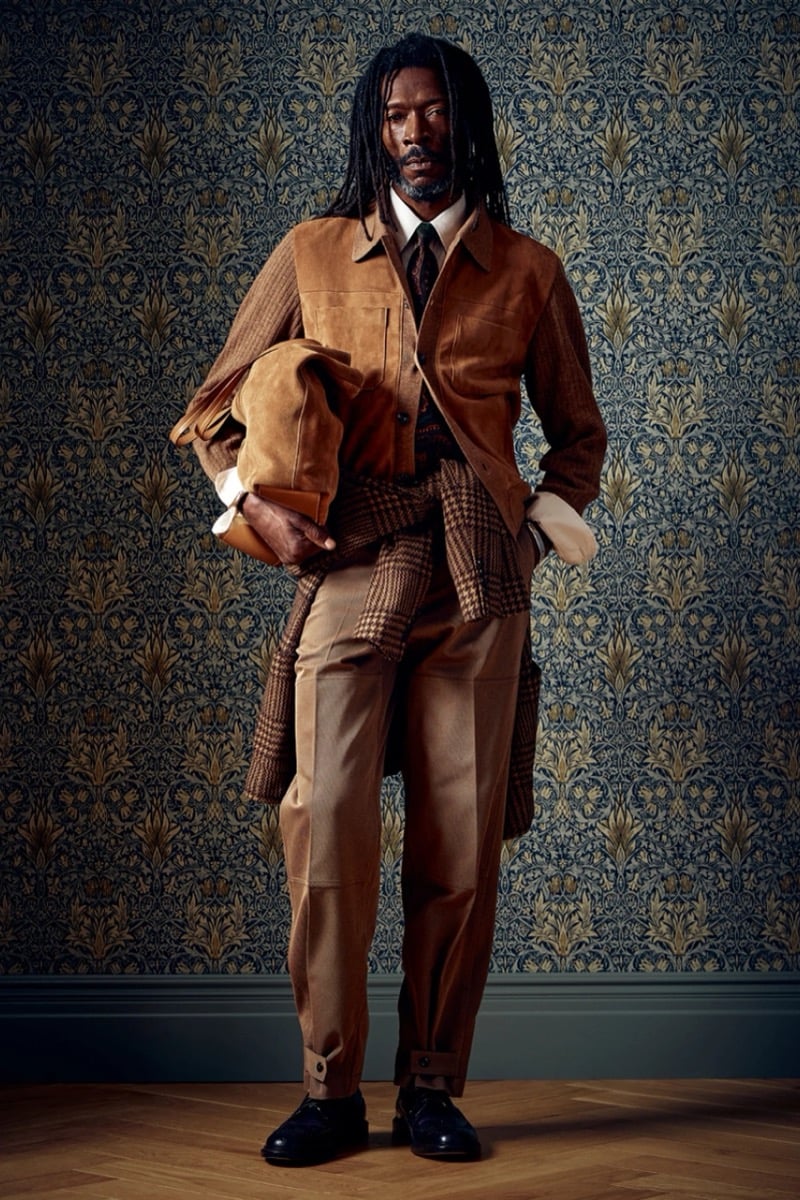 Man in a tan suede jacket with a houndstooth wrap tied at the waist and a tan bag underarm, for Todd Snyder Fall 2026