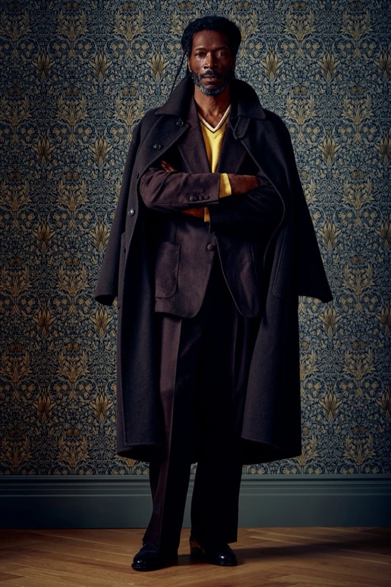 Man with arms crossed in an oversized dark wool coat over a yellow sweater, for Todd Snyder Fall 2026