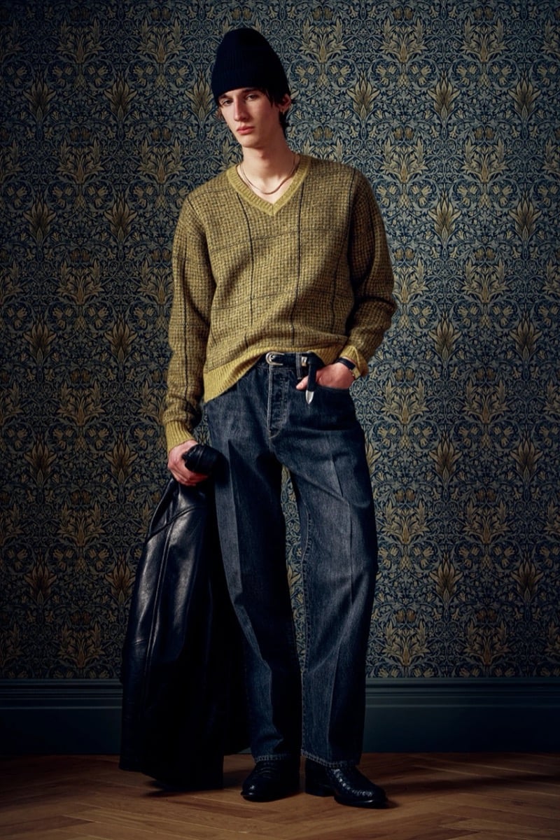 Man in an olive knit sweater and dark jeans, holding a leather jacket, for Todd Snyder Fall 2026