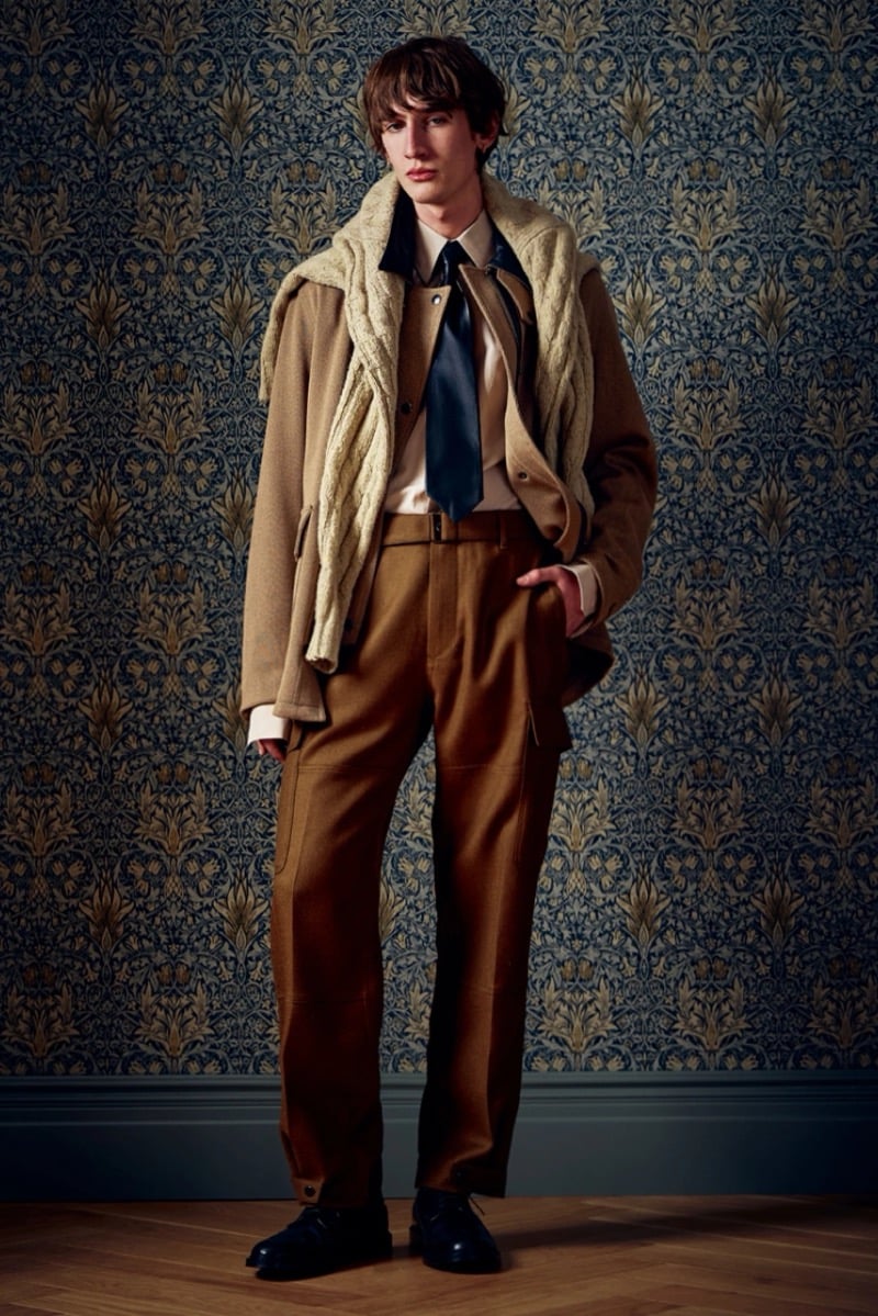 Man in a camel coat with a cable-knit scarf draped over the shoulders and a dark tie, for Todd Snyder Fall 2026