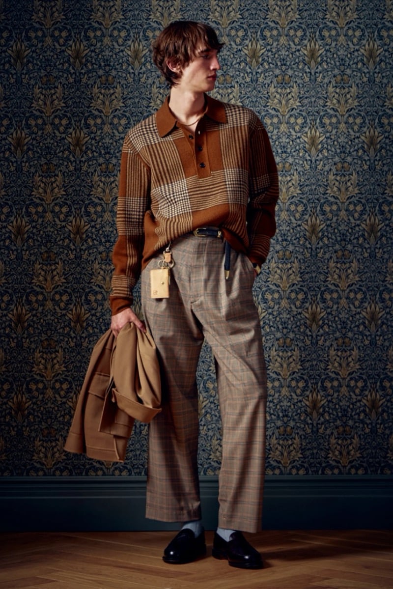 Man in a plaid polo sweater and matching plaid trousers, holding a camel coat, for Todd Snyder Fall 2026