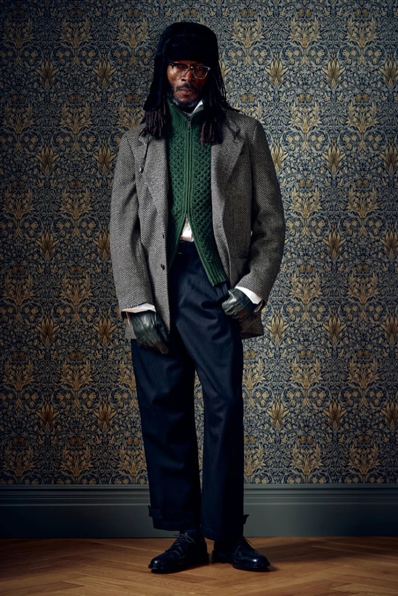 Man in a herringbone wool blazer over a green cable-knit sweater, wearing gloves and a trapper hat, for Todd Snyder Fall 2026