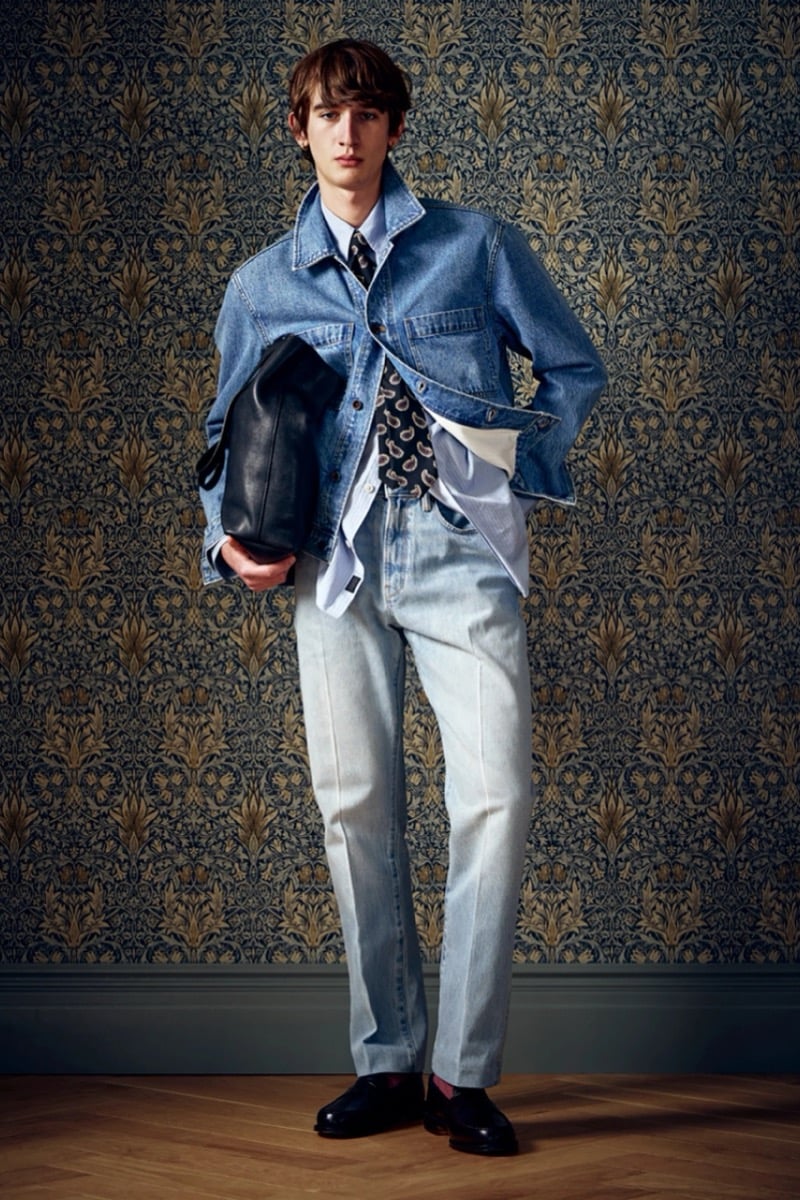 Man in a light denim jacket and a patterned tie over light jeans, carrying a black bag, for Todd Snyder Fall 2026