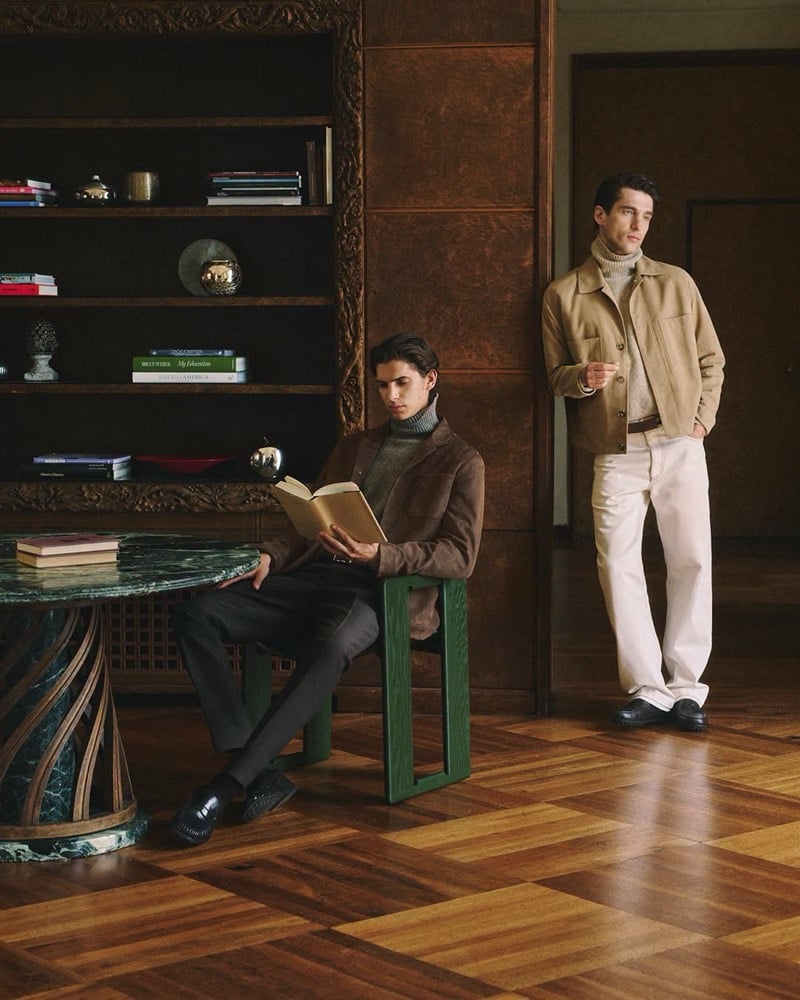 Hedi Ben Tekaya reads in a brown suede jacket and gray rollneck while Anatol Modzelewski stands nearby in a tan suede overshirt in a wood-panelled library for Tod's fall-winter 2026 campaign