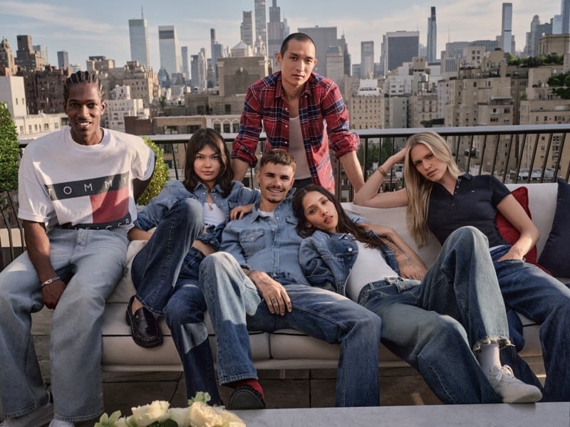 Romeo Beckham sits at the center of a six-person cast including Yasmin Wijnaldum in denim jackets and jeans on a rooftop couch, with the Manhattan skyline glowing behind them