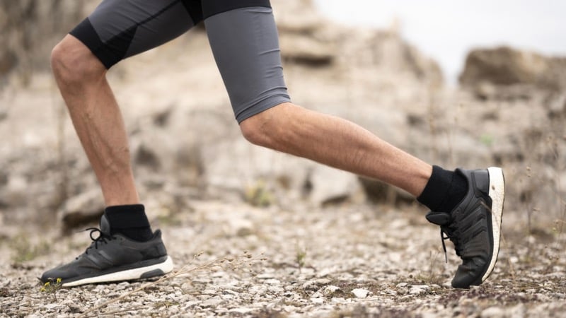 A close-up of a runner's legs mid-stride in black trail running shoes on a gravel path