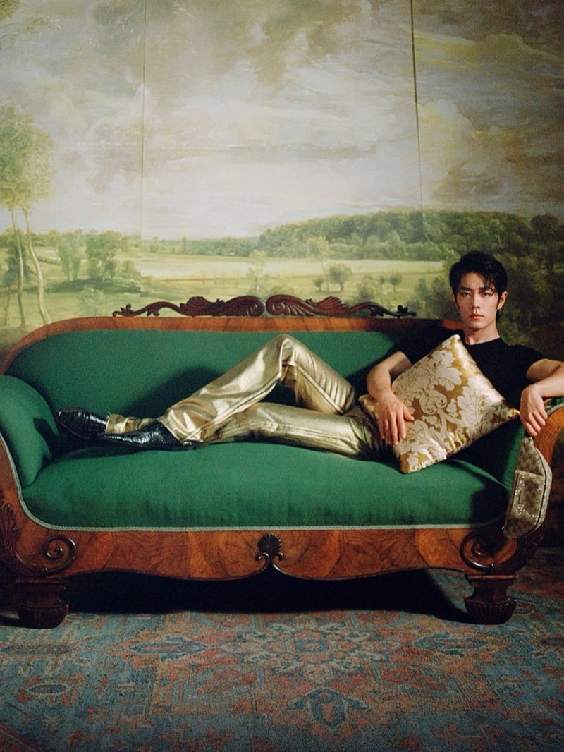 Xiao Zhan reclines on a green sofa in gold metallic trousers and a dark top for Gucci's Primavera campaign