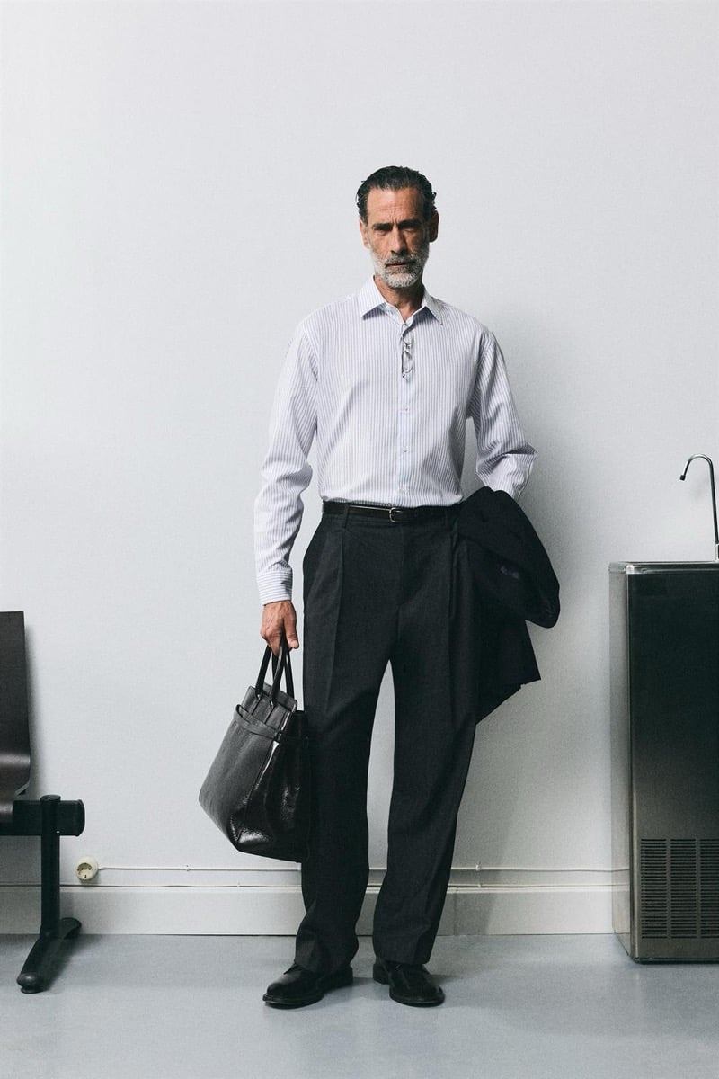 John Armstrong wears a striped shirt and dark trousers, a leather tote bag in hand and jacket over his arm, for Zara's back to work 2026 campaign