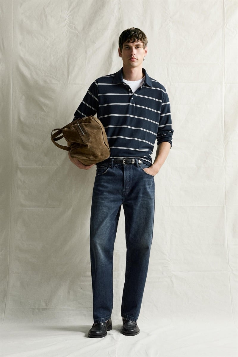 Jegor Venned in a striped knit polo holding a suede tote bag over dark denim