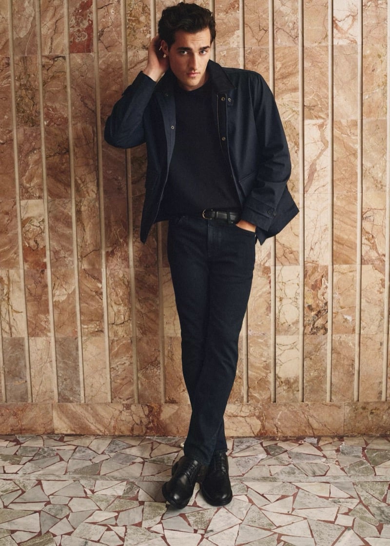 Adam Sattrup stands against a marbled wall in a collared jacket over a crewneck sweater with slim indigo jeans and black derby shoes, for Mango's Superior Denim collection