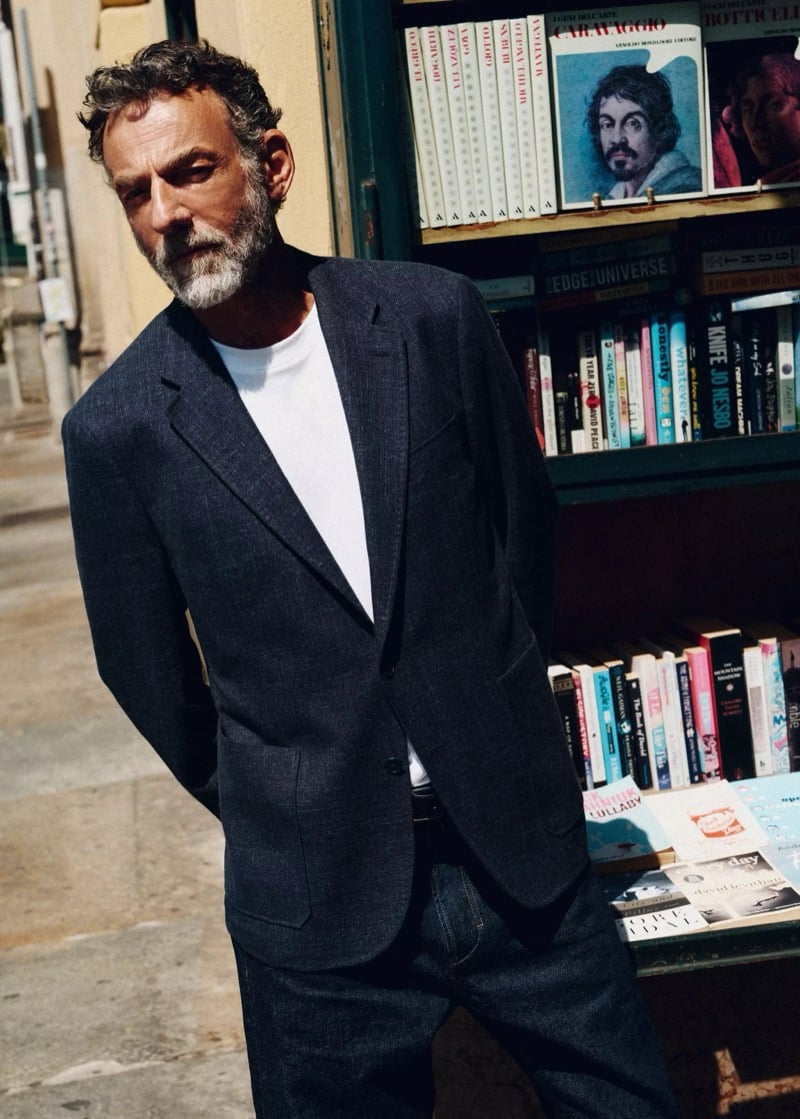 Alain Gossuin stands outside a bookshop in a charcoal wool-cotton-denim blazer over a tee with dark trousers, for Mango's Superior Denim collection