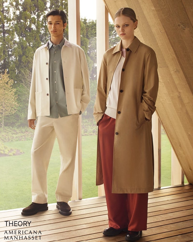 Ruben Bilan-Carroll in a cream chore jacket over a sage shirt with cream trousers and brown suede shoes, next to Ava Shipp in a camel car coat over rust wide-leg trousers, on a wooden porch for Theory