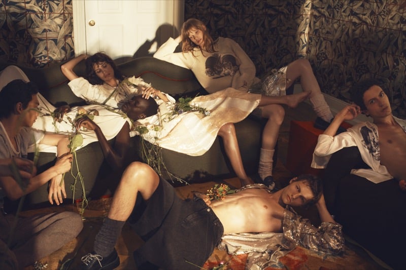 Bai, Roman Lenoir, and Takfarines Bengana lounging with other models among loose flowers in a room with leaf-print wallpaper, Roman shirtless on the floor
