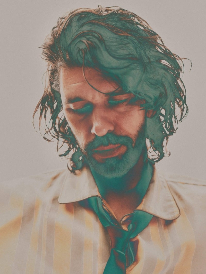 Hazy green-tinted double exposure of Ben Whishaw with eyes closed and head bowed, wearing a glossy striped shirt and knotted tie