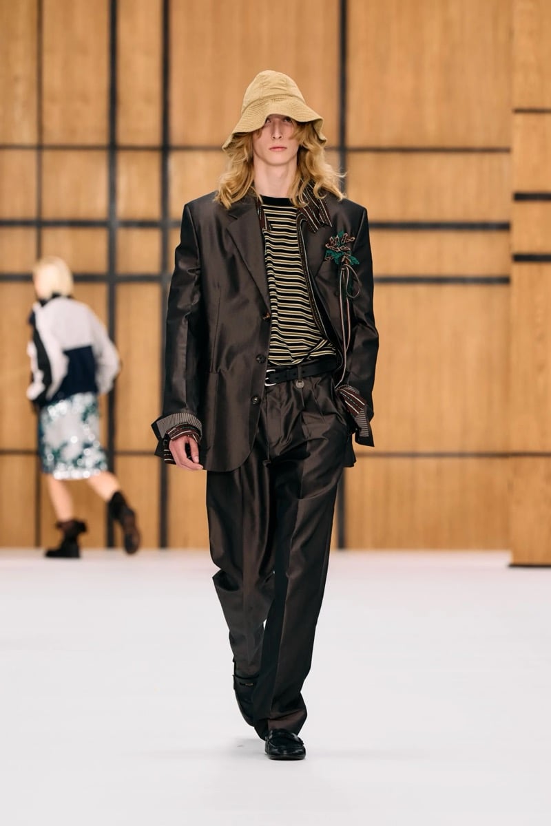 A model in a bucket hat and satin suit over a striped top, finished with a brooch, for Burberry's summer 2027 collection