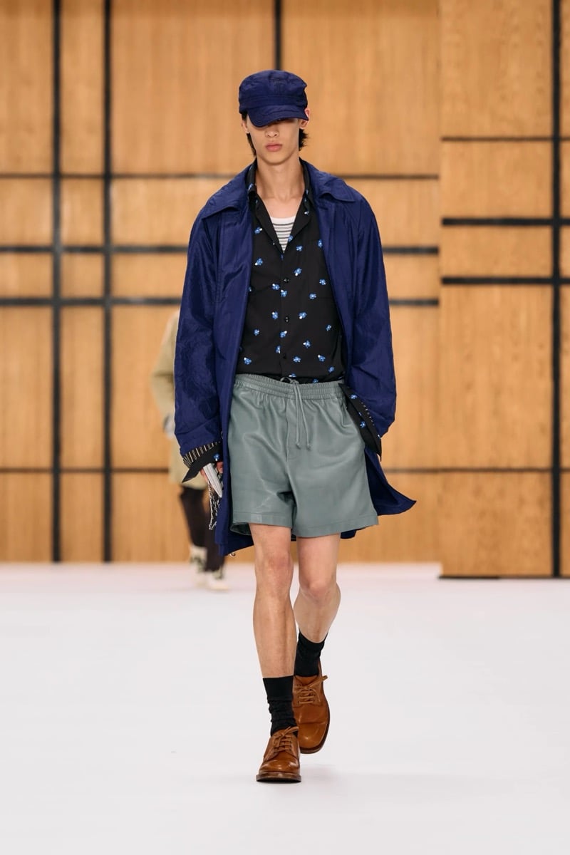 A model in a cap and lightweight coat over a printed shirt, with leather shorts and loafers, for Burberry's summer 2027 collection