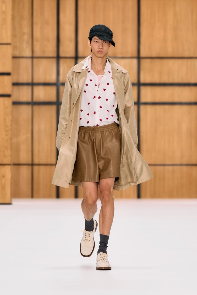 A model in a cap and lightweight car coat over a floral print shirt, with leather shorts, for Burberry's summer 2027 collection