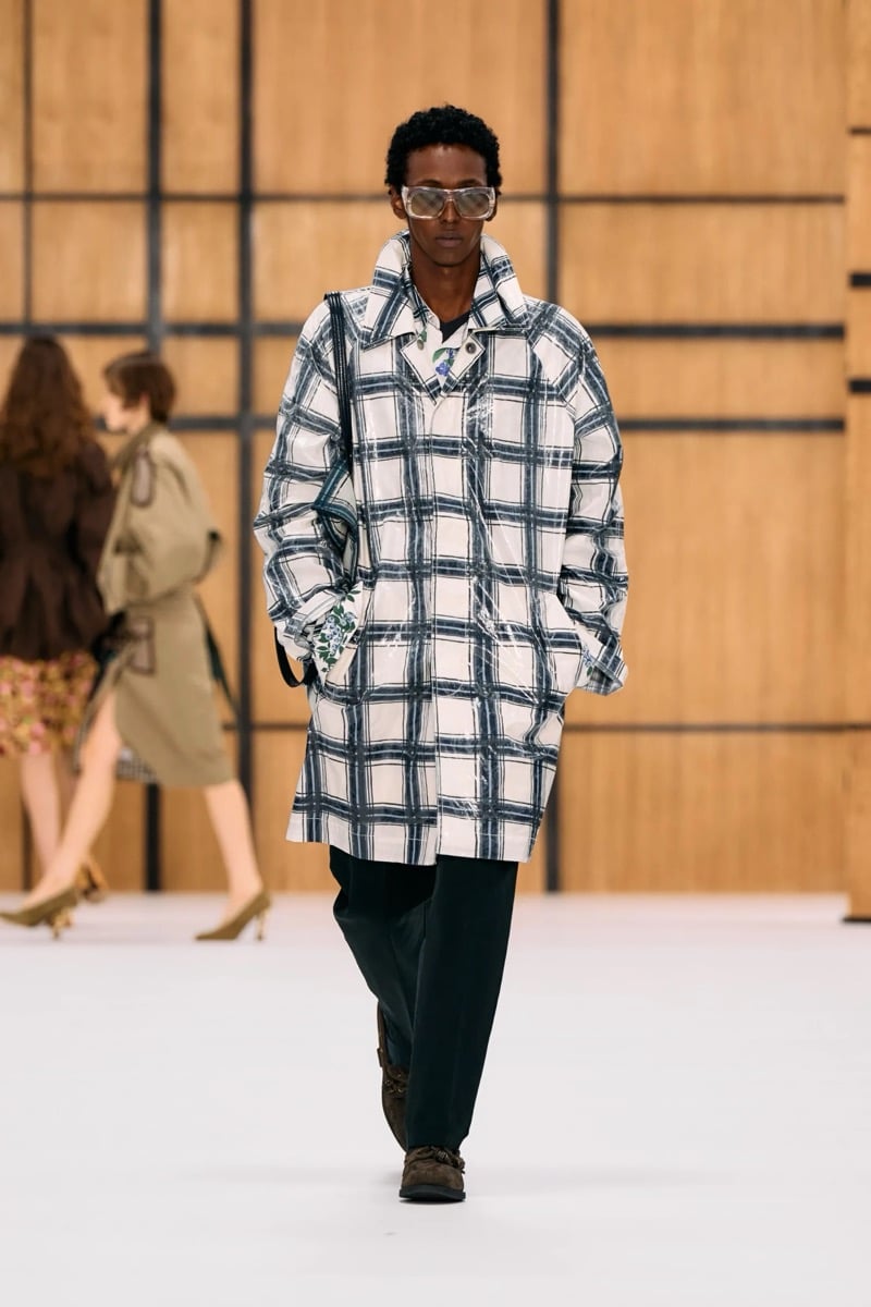 A model in sunglasses and a coated check car coat, with trousers and suede shoes, for Burberry's summer 2027 collection