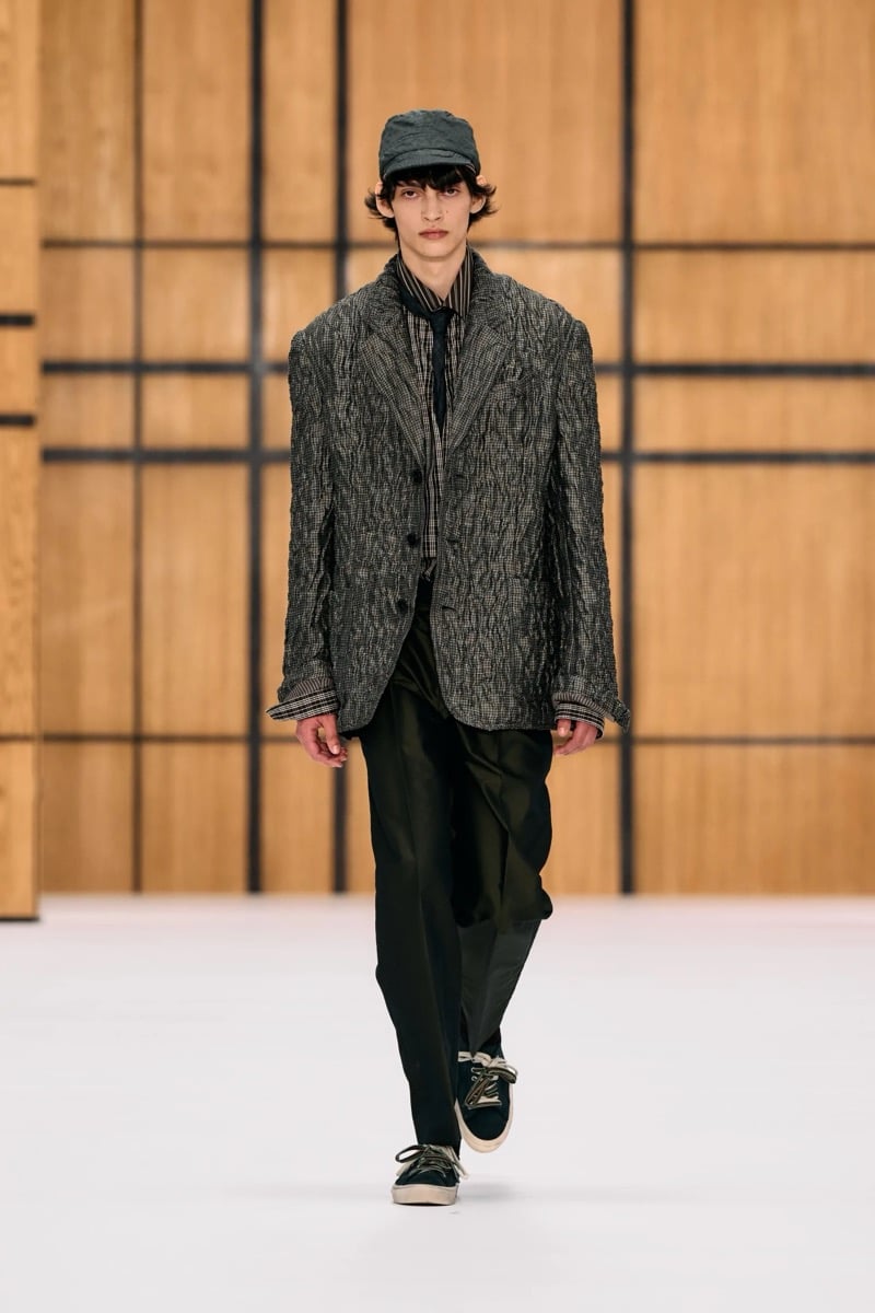 A model in a cap and crinkled check blazer over a check shirt and tie, with trousers and sneakers, for Burberry's summer 2027 collection