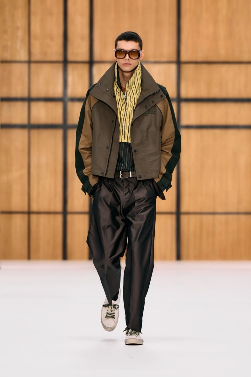 A model in sunglasses and a cropped paneled jacket over a yellow striped shirt, with pleated trousers, for Burberry's summer 2027 collection