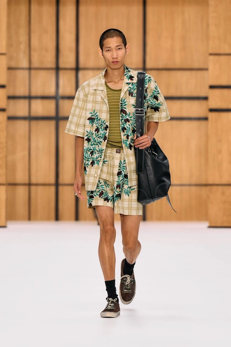 A model in an embroidered check camp shirt and matching shorts, with a leather bucket bag, for Burberry's summer 2027 collection