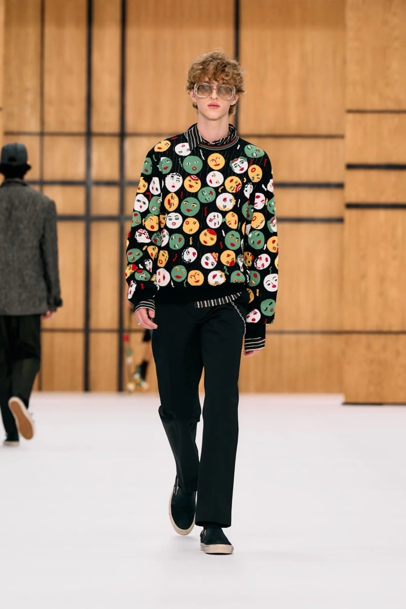 A model in a knit sweater covered in illustrated faces, with trousers and sneakers, for Burberry's summer 2027 collection