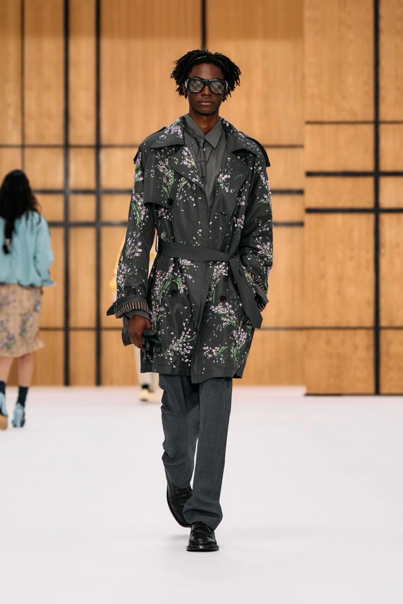 A model in sunglasses and a floral print trench coat over a shirt and tie, with check trousers, for Burberry's summer 2027 collection