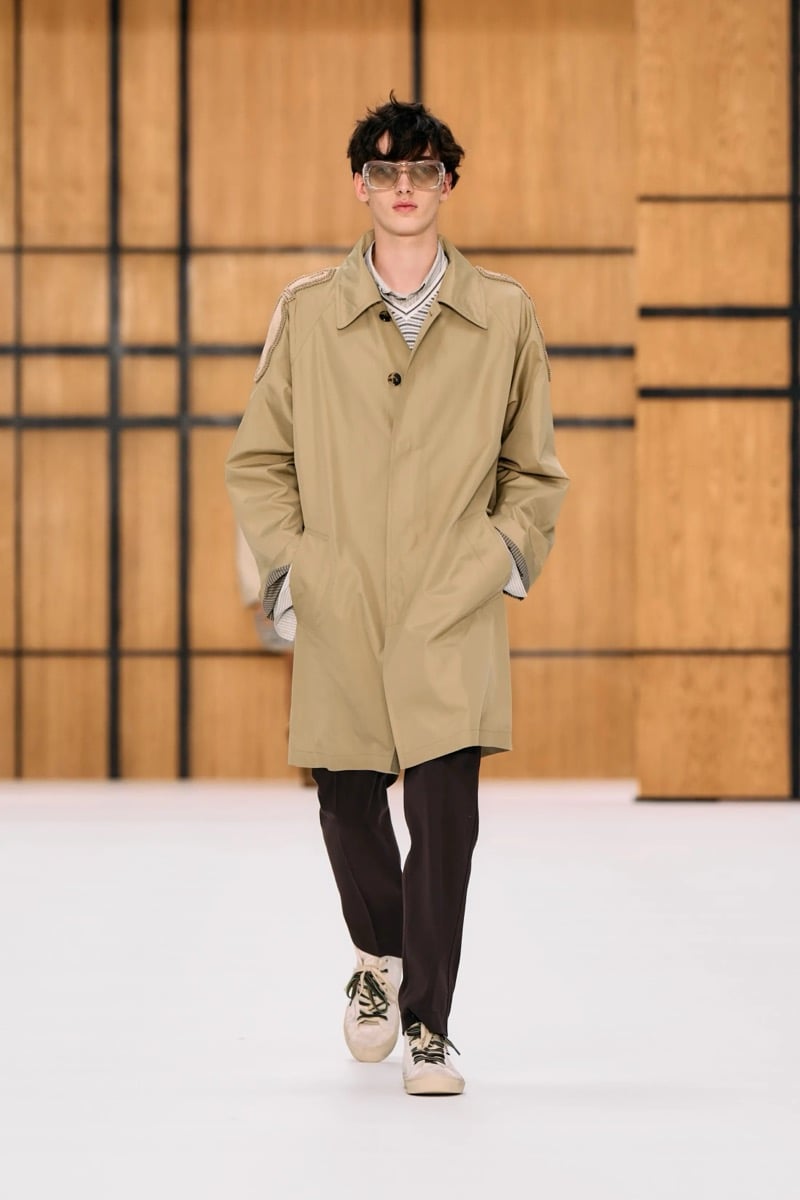 A model in tinted sunglasses and a khaki car coat over a striped shirt, with trousers and sneakers, for Burberry's summer 2027 collection