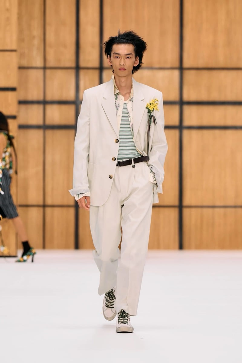 A model in a light-colored suit over a striped tank and floral shirt, with a yellow flower on the lapel, for Burberry's summer 2027 collection