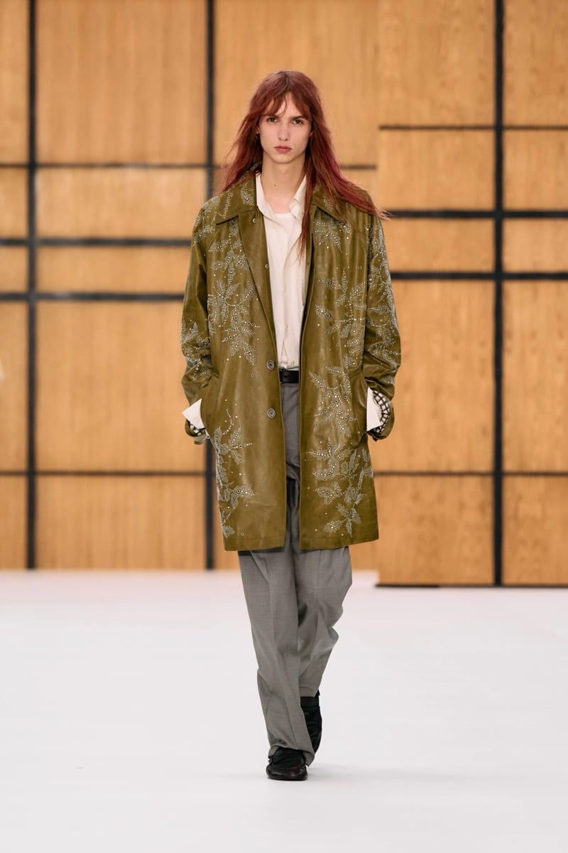 A model in an olive leather coat with floral embellishment, worn with a shirt and gray check trousers, for Burberry's summer 2027 collection