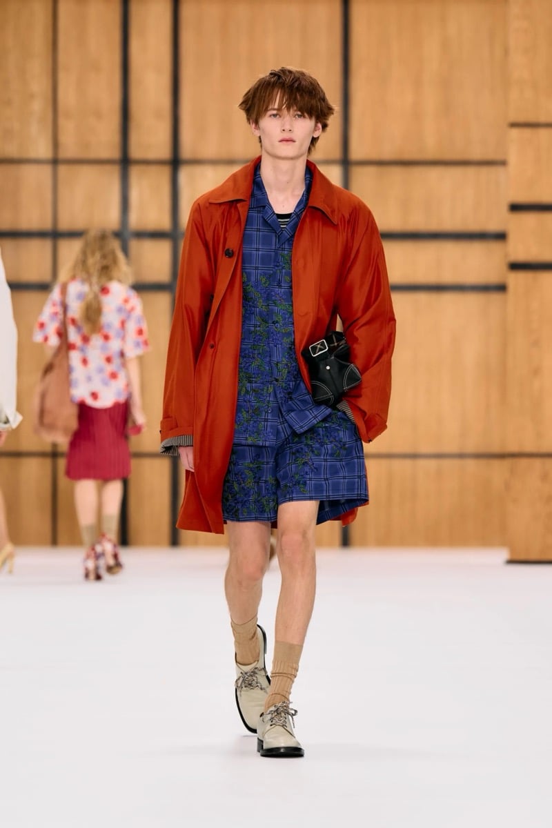 A model in a rust coat over an embroidered check shirt and matching shorts, for Burberry's summer 2027 collection
