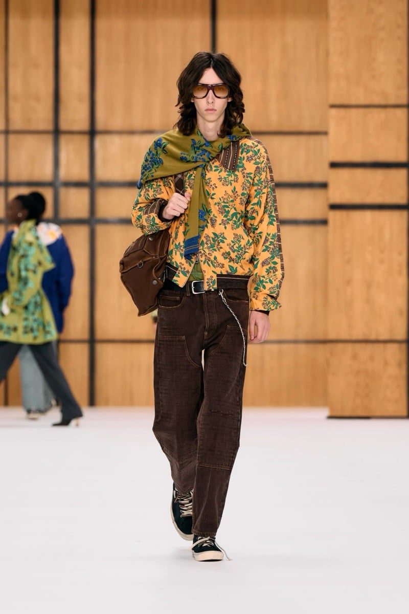 A model in a yellow floral bomber jacket and printed scarf, with brown jeans and a leather bag, for Burberry's summer 2027 collection
