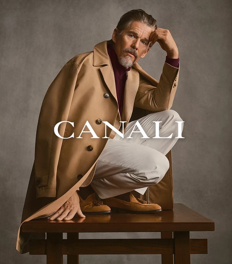Ethan Hawke crouches on a wooden bench in a camel trench coat for Canali's fall-winter 2026 campaign.