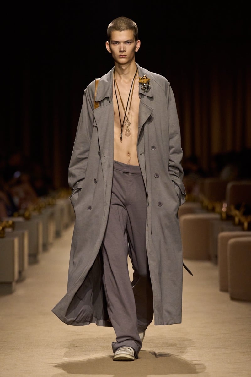 A model in an oversized gray trench coat worn open over a bare chest with slouchy gray trousers, for Coach's spring 2027 collection