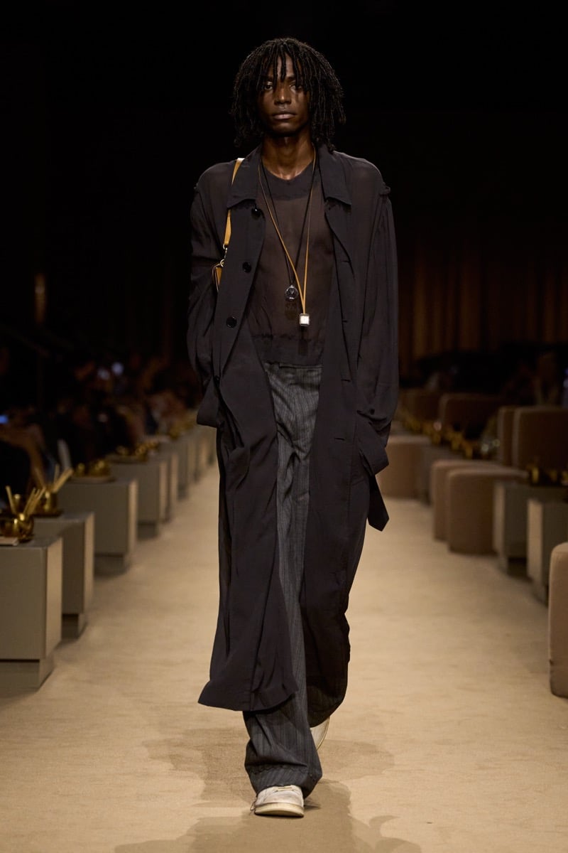 A model in a sheer black duster over a sheer top with wide pinstripe trousers, for Coach's spring 2027 collection