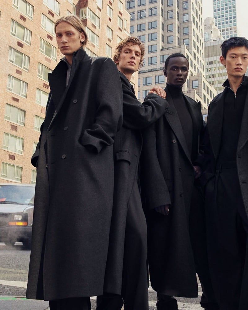 Jesse Rinderknecht, Leon Dame, Malick Bodian, and Hoyong Kim stand close together in long dark coats on a New York street, for COS's fall 2026 campaign