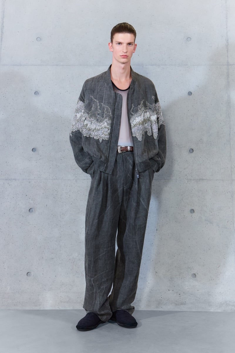 A model in a beaded bomber jacket over a sheer top, with belted pleated trousers, for Emporio Armani's spring-summer 2027 collection
