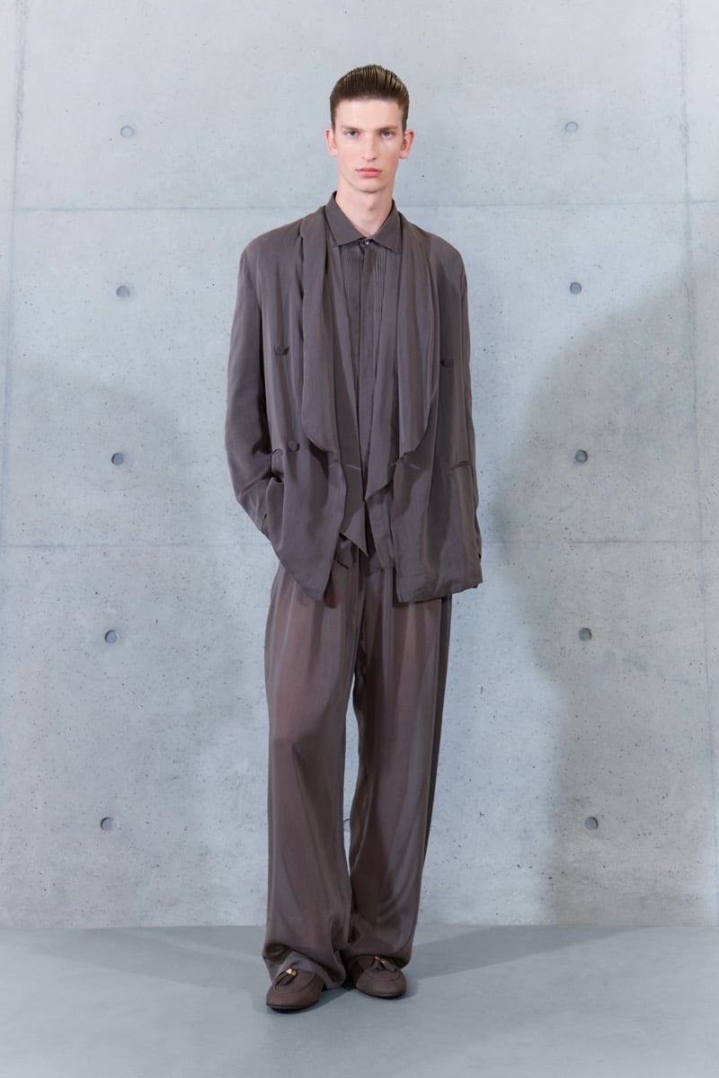 A model in a fluid brown jacket with draped lapels over a pintucked shirt, with sheer trousers, for Emporio Armani's spring-summer 2027 collection