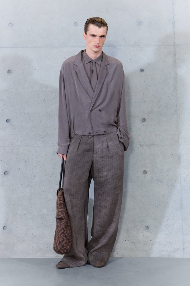 A model in a cropped wrap jacket over a shirt and tie, with pinstripe pleated trousers and a woven bag, for Emporio Armani's spring-summer 2027 collection