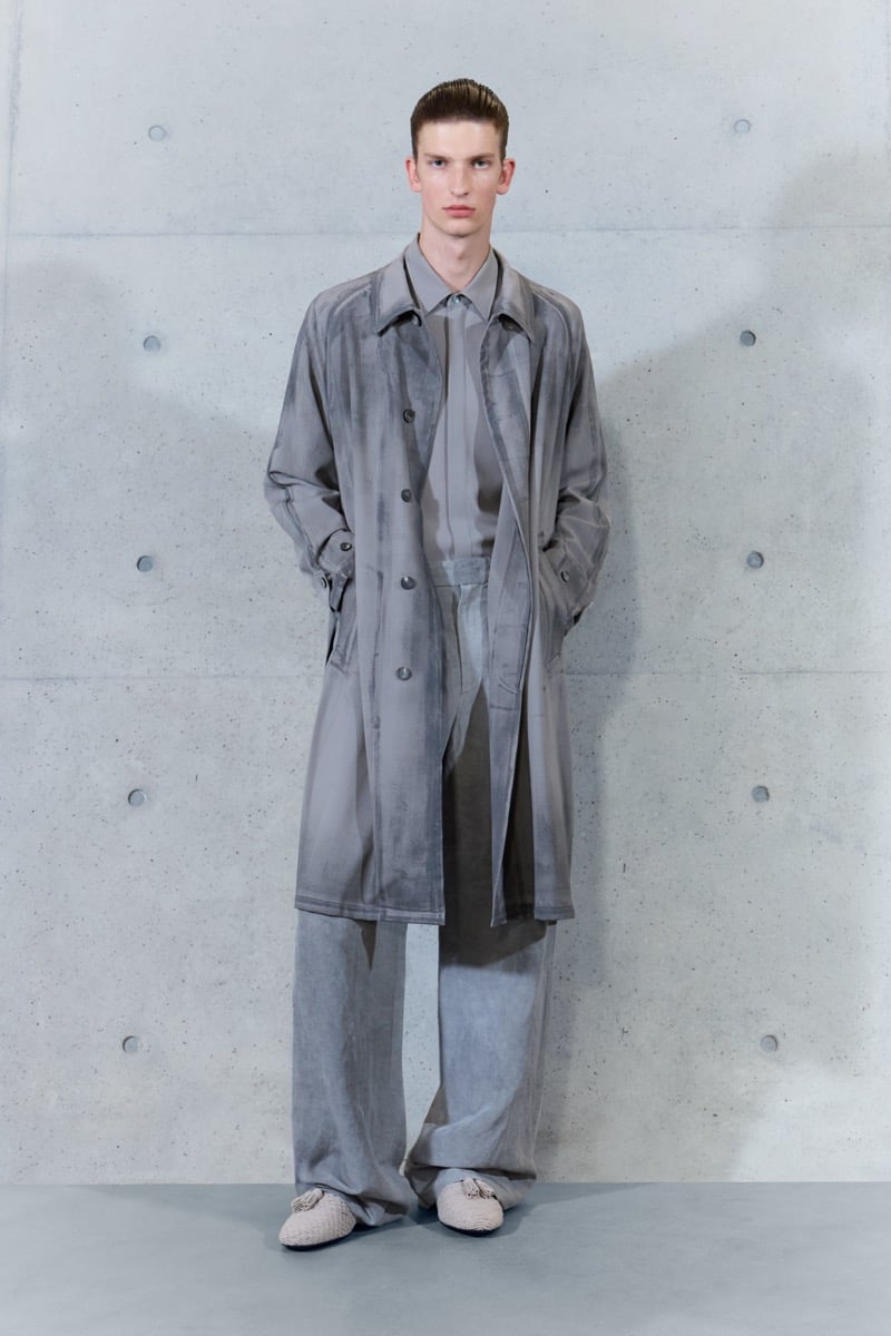 A model in a faded gray trench coat over a shirt, with wide-leg trousers, for Emporio Armani's spring-summer 2027 collection