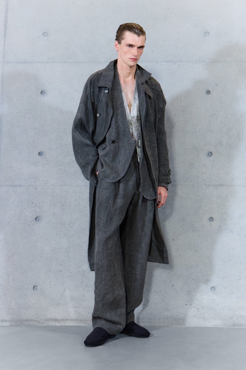 A model in a gray coat over a jacket and chainmail vest, with wide-leg trousers, for Emporio Armani's spring-summer 2027 collection
