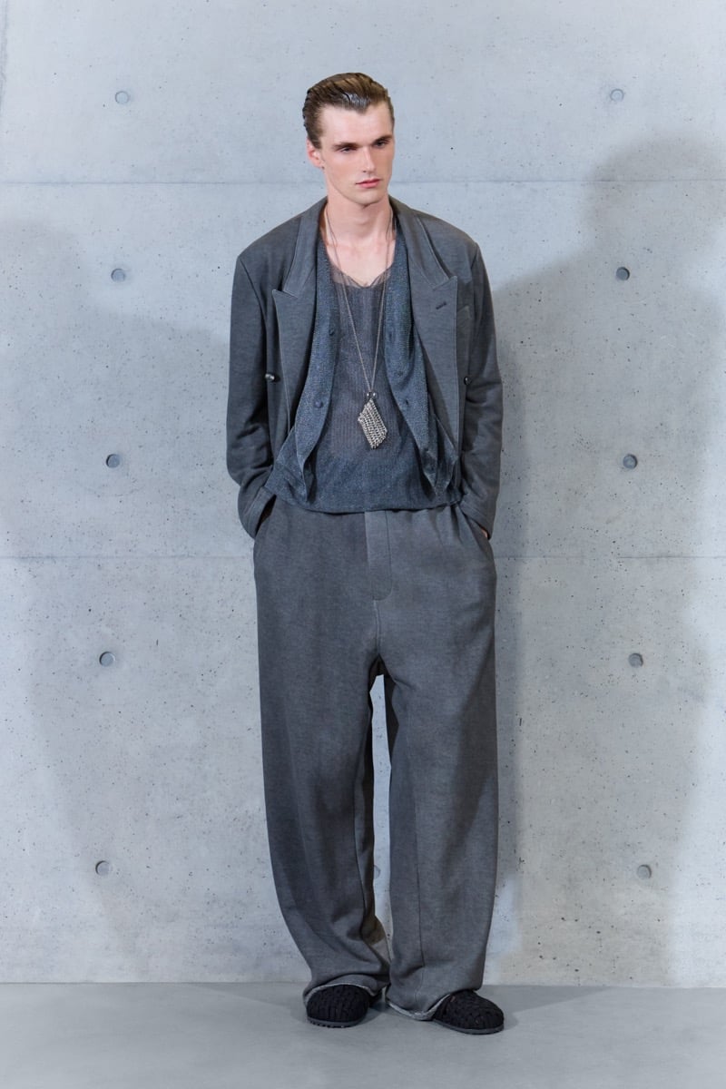 A model in a gray double-breasted jacket over sheer layers, with wide-leg trousers and a pendant necklace, for Emporio Armani's spring-summer 2027 collection