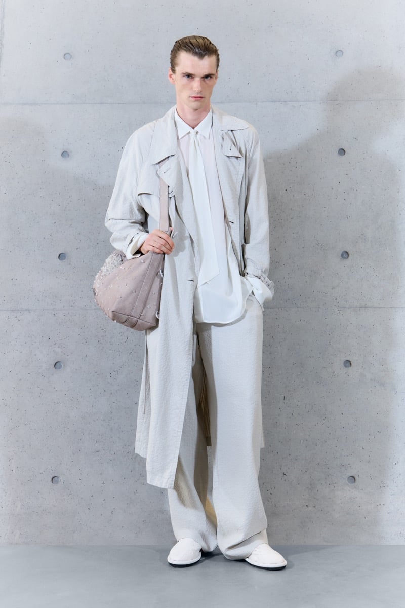 A model in a lightweight trench coat over a shirt and narrow scarf, with wide-leg trousers and a studded shoulder bag, for Emporio Armani's spring-summer 2027 collection